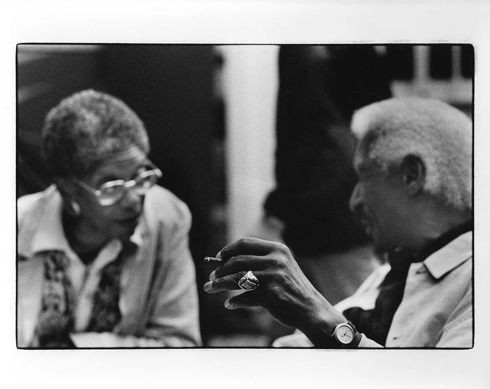 Two people leaning toward one another in conversation, photographed in black and white