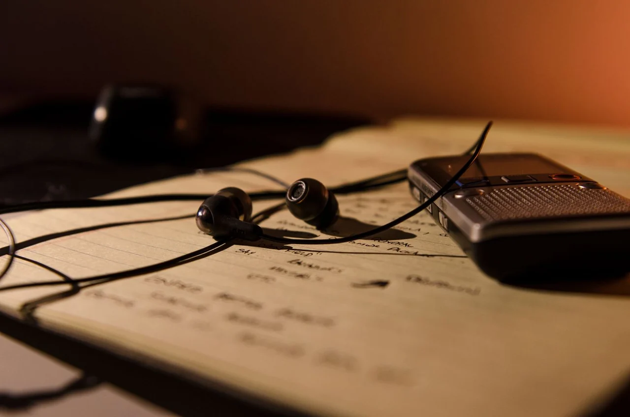 A voice recorder and earphones resting on handwritten notes
